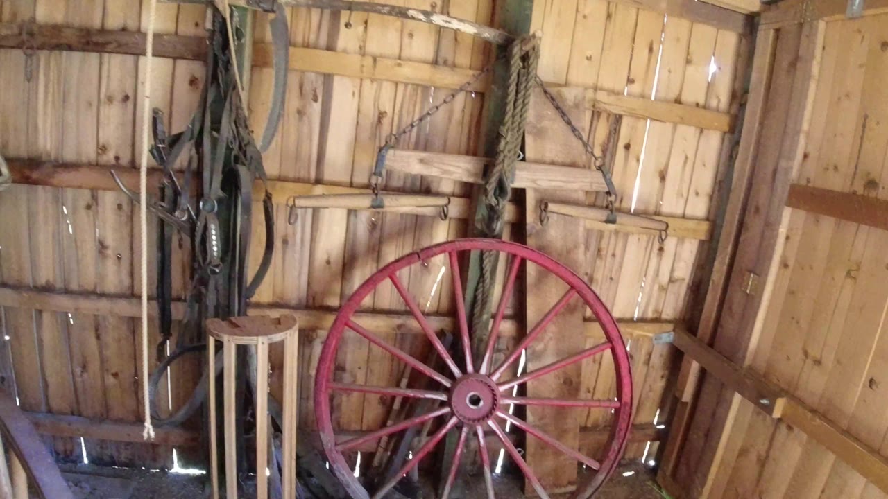 Weathered red wheel fills the lower right of a wooden shed interior in Winter Park, Colorado, with hanging straps and no visible people.