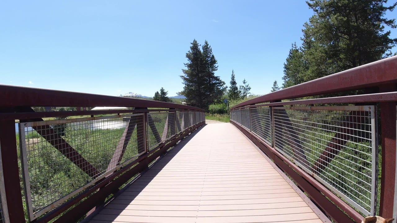 The bridge walkway continues straight ahead in Winter Park, Colorado, framed by red railings and wire mesh with trees and no visible people.