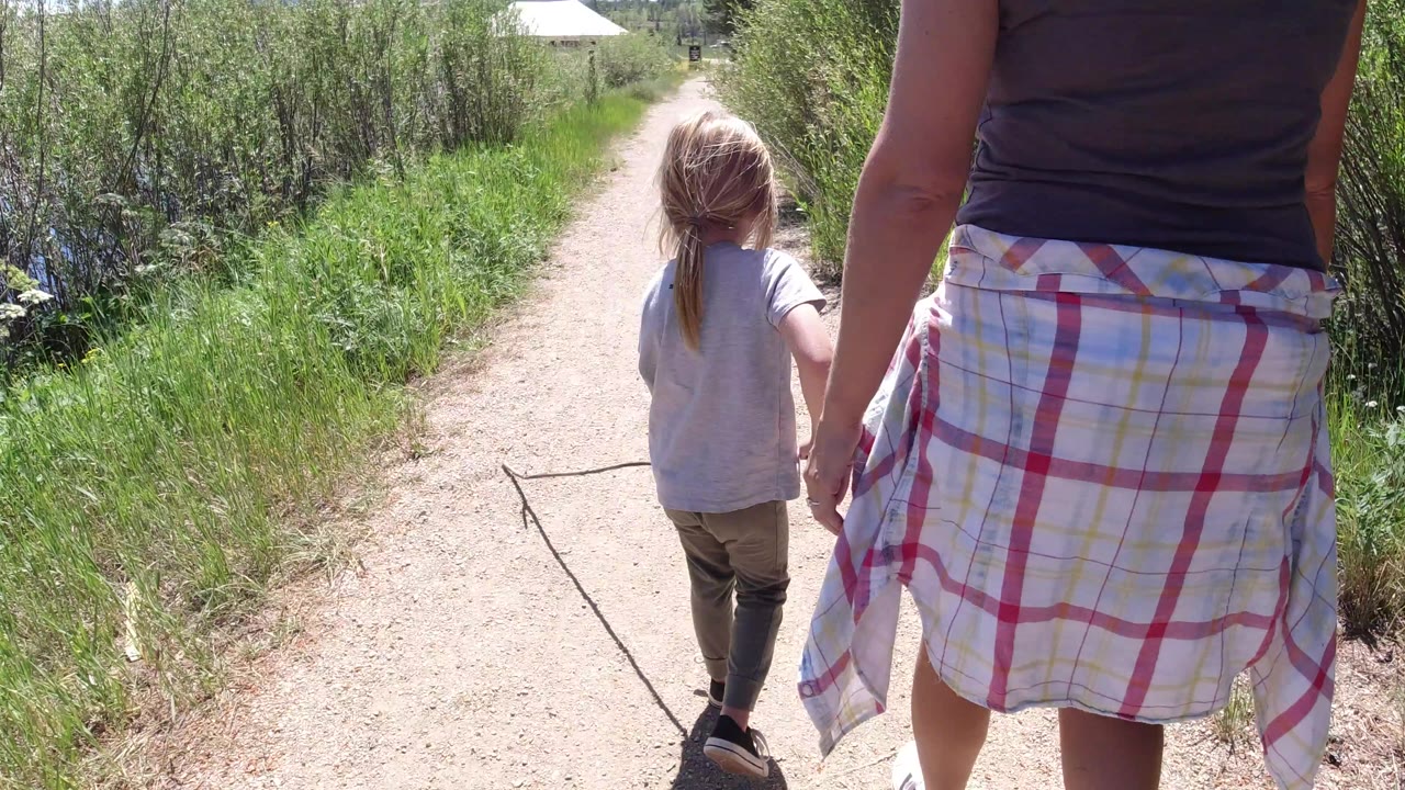 The adult fills more of the right foreground while the child continues ahead on the Winter Park dirt trail between green vegetation.