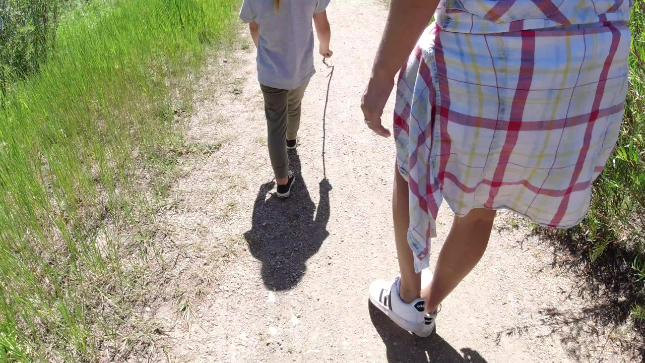 Adult and child walking on a narrow dirt path through green grass.