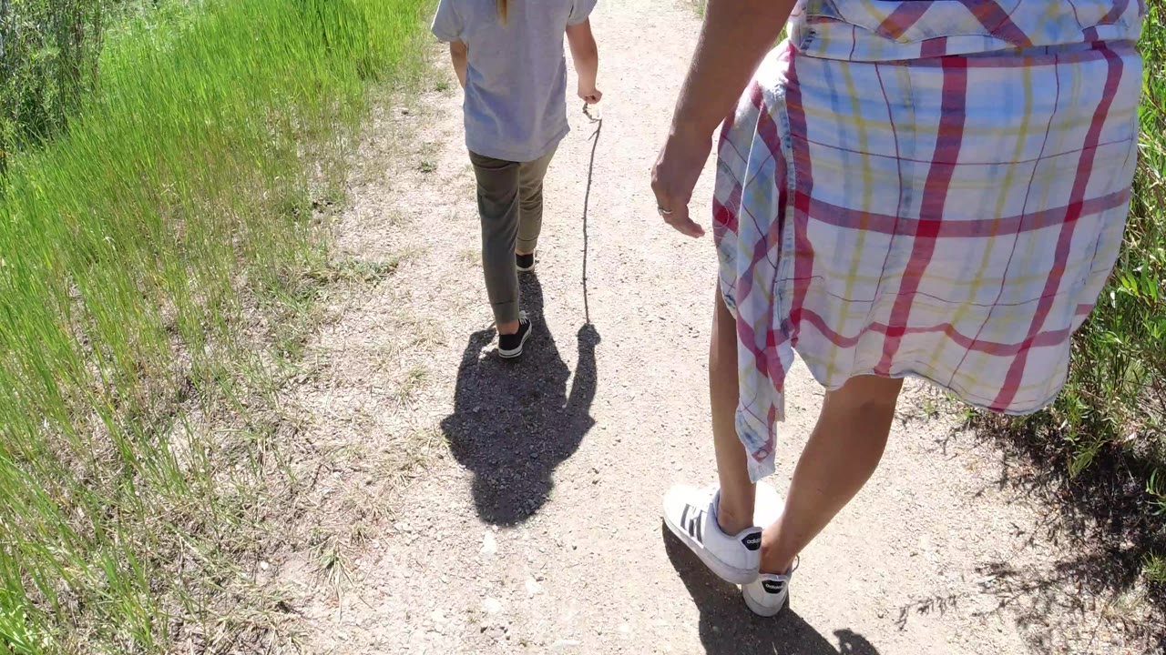 The child walks ahead while the adult woman's skirt and legs fill the right foreground on a bright path in Winter Park, Colorado.
