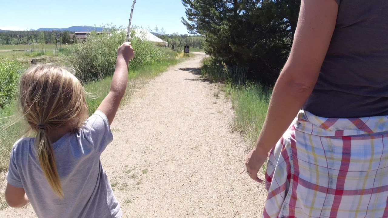 Blonde child and cropped adult walking on a dirt trail.