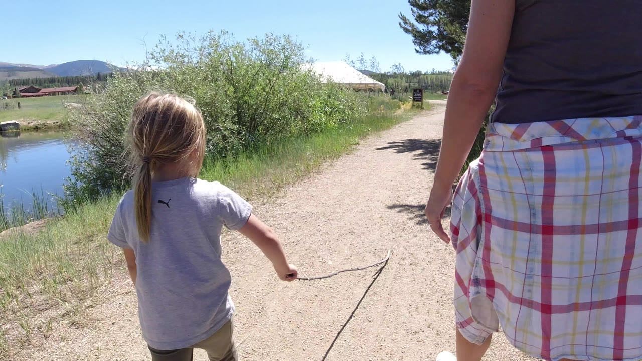 Child and adult walking beside a pond on a gravel path