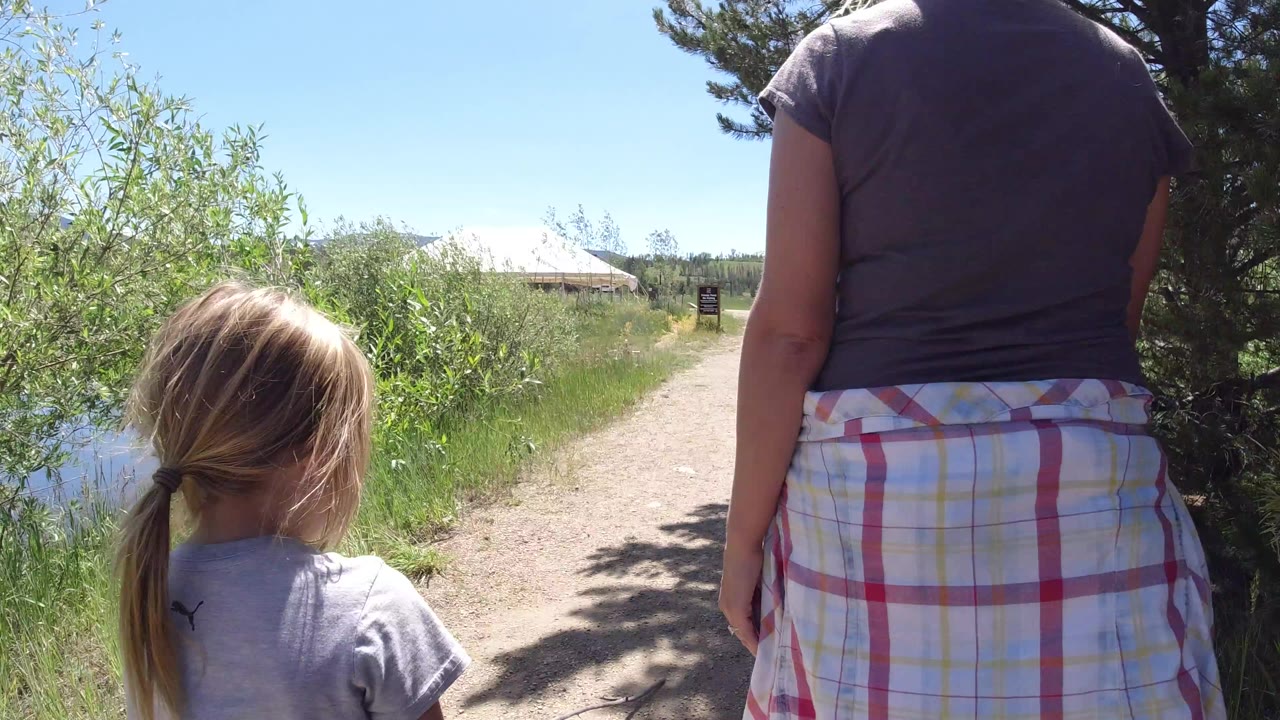 Woman and young girl walking away on a dirt path beside greenery.