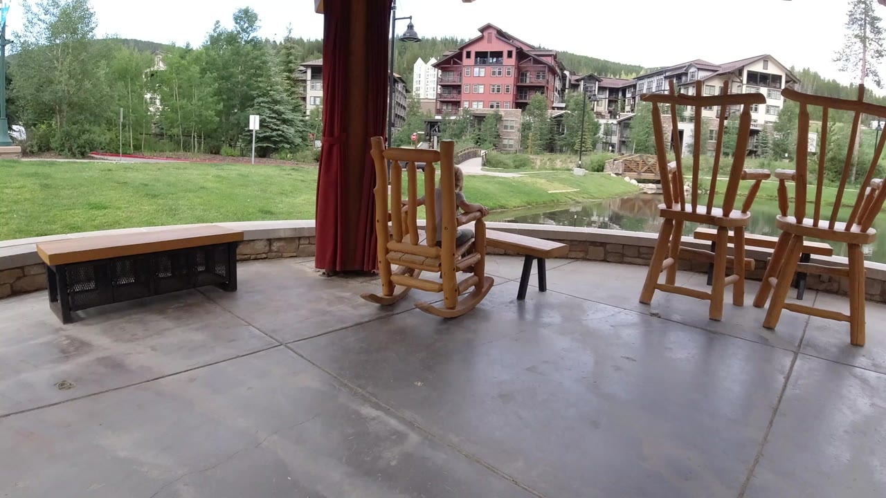 Covered patio with wooden rocking chairs facing a pond and lodge buildings.