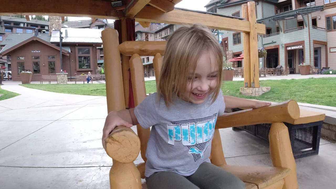 Young girl smiling in a wooden rocking chair outdoors.