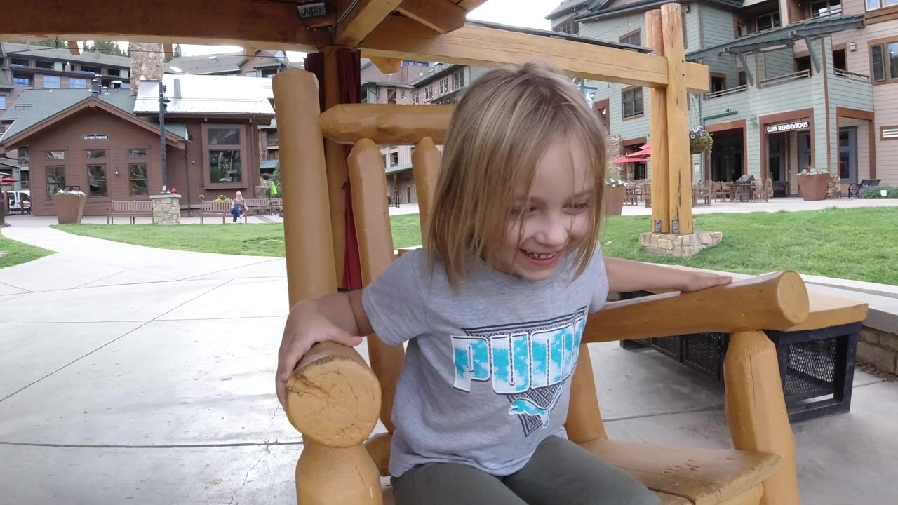 The child leans forward with both hands on the wooden chair arms in the Winter Park courtyard setting.