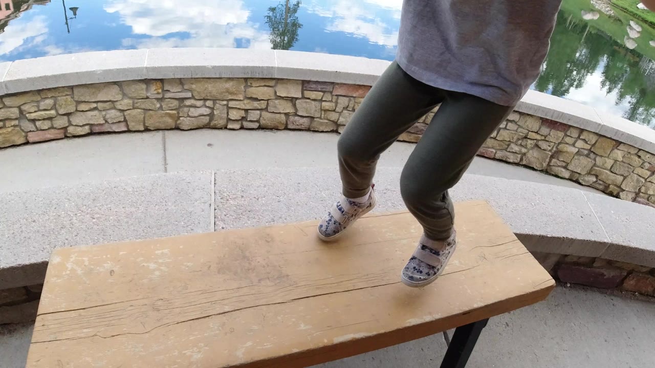 Child's legs on a small wooden table beside a lake patio.