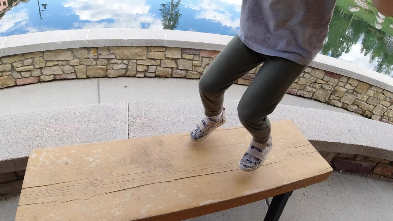 The child shifts her feet on the wooden table while the low stone wall and still lake fill the background in Winter Park, Colorado.