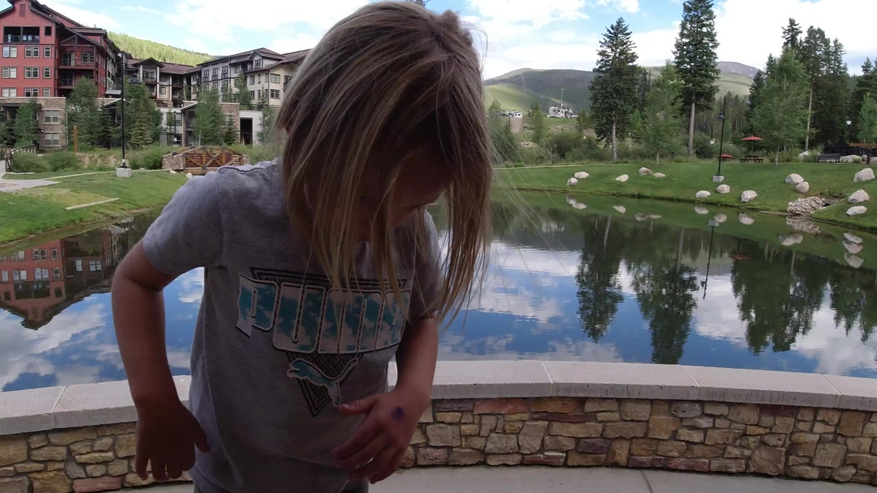 Young child beside a reflective lake and resort buildings.