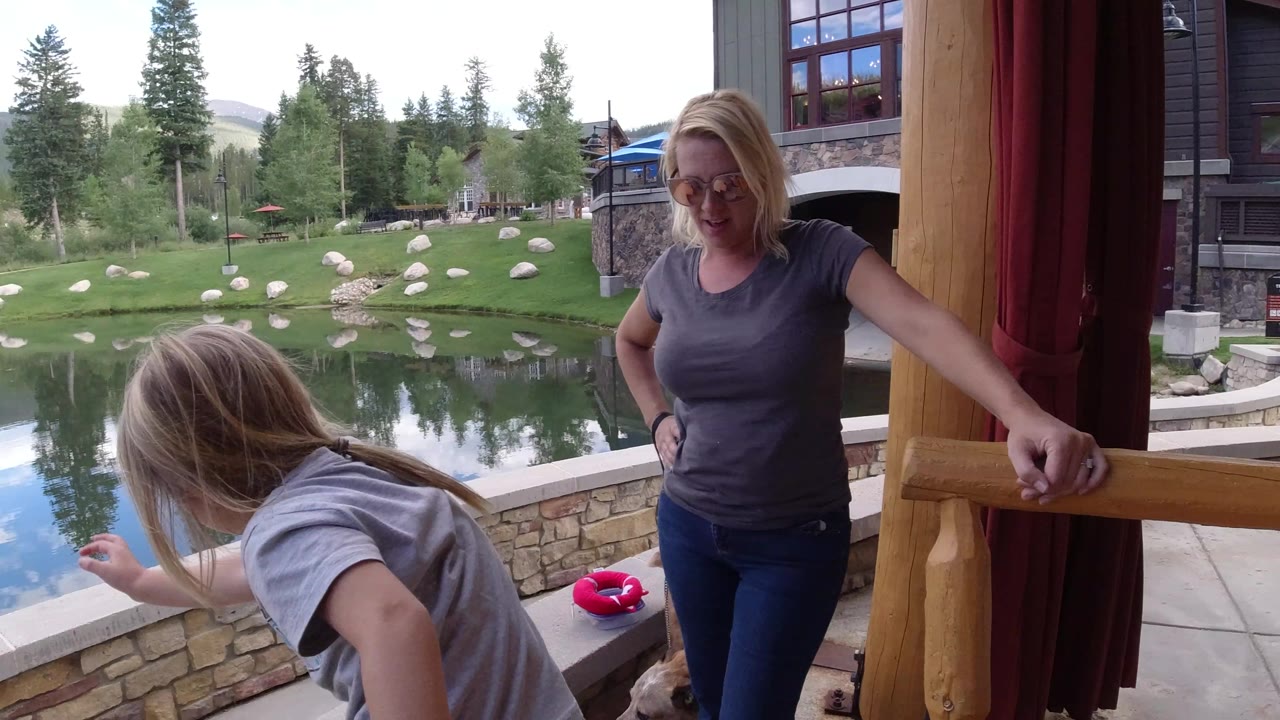 The young girl bends toward the patio edge while the adult woman watches near the doorway, with the Winter Park pond, grass, rocks, trees, and buildings behind them.
