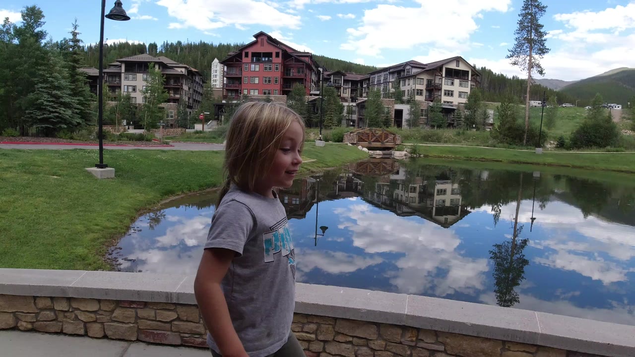 Young girl walking beside a pond with lodge buildings reflected in the water.