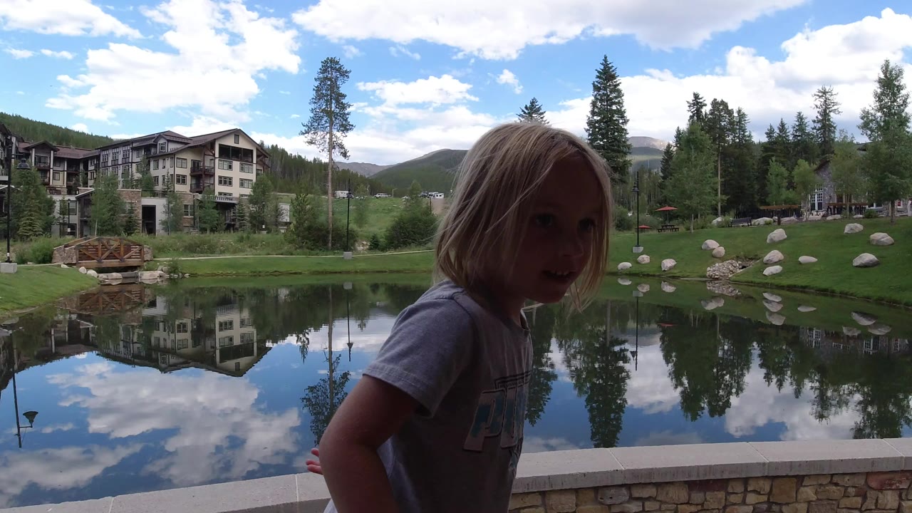 Young girl beside a reflective lake and lodge buildings.