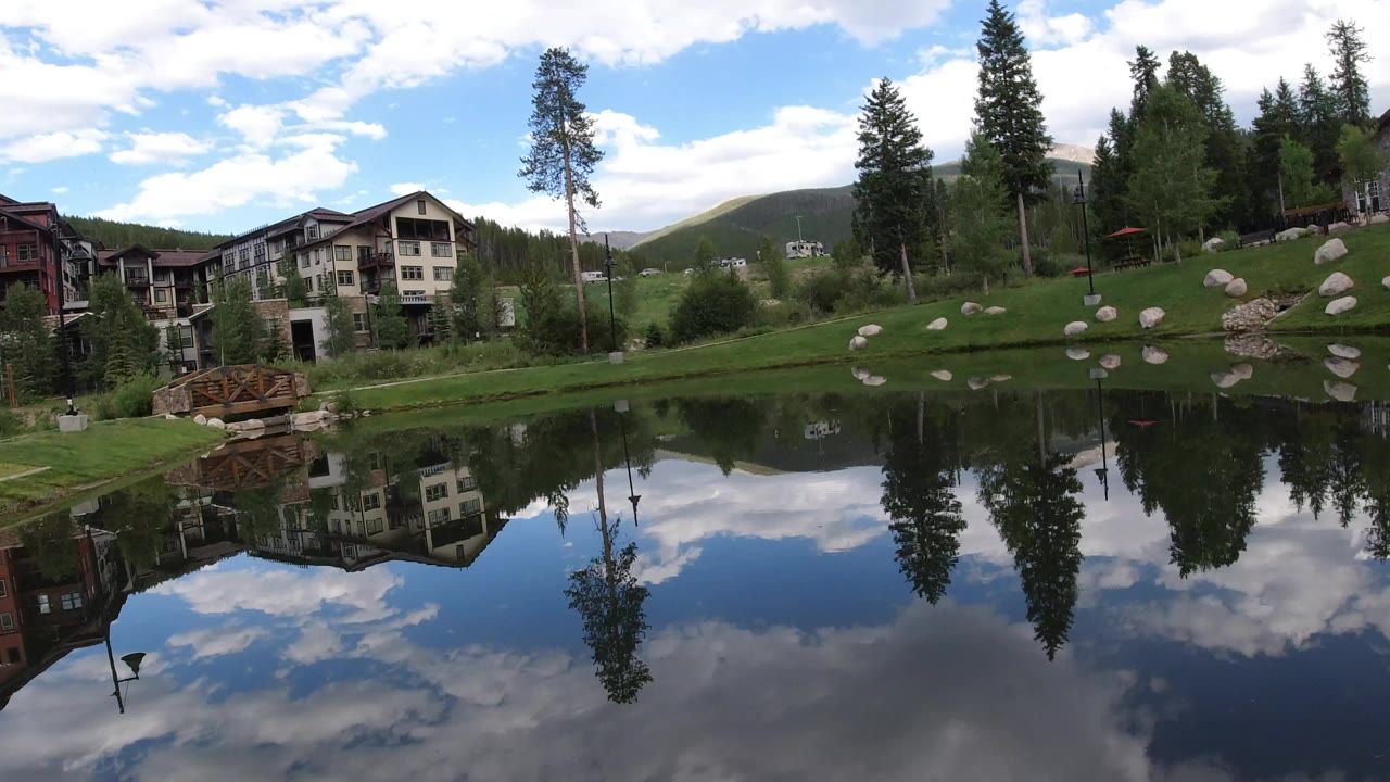 Pond reflecting buildings, evergreens, clouds, and sky