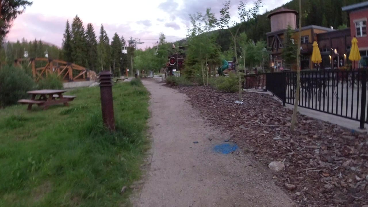 Curving path with picnic table, small trees, rock bed, fencing, and buildings.
