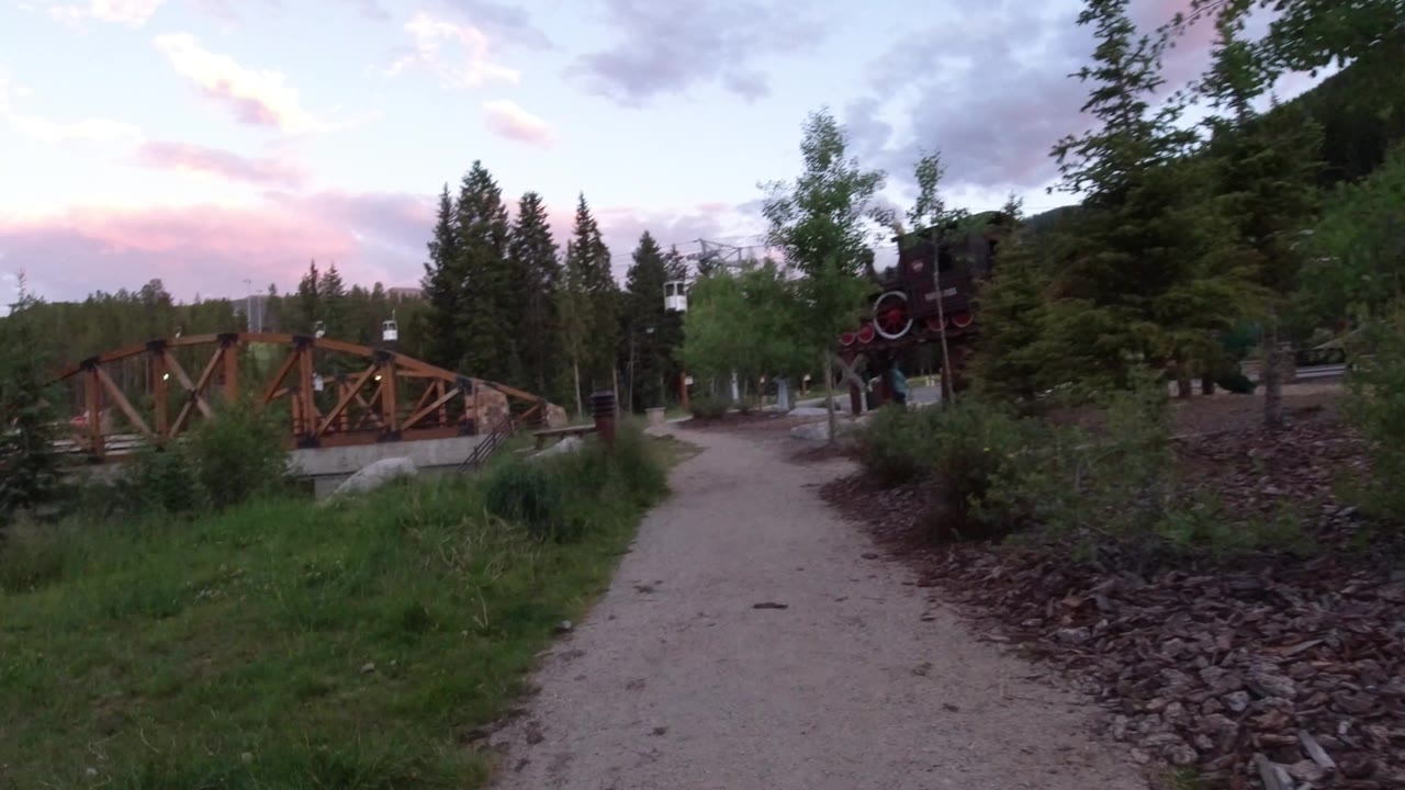 Curving village path with wooden bridge and rail-style structure nearby
