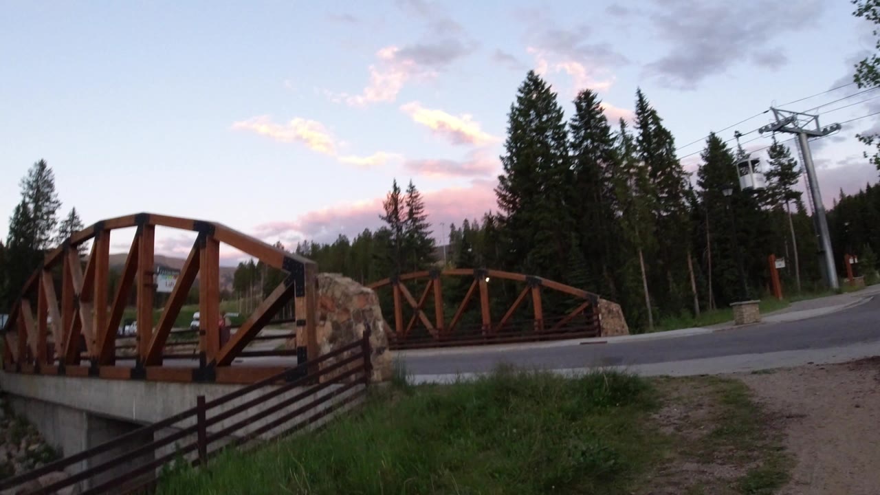 Wooden bridge beside a curving road with pine trees and ski lift towers.