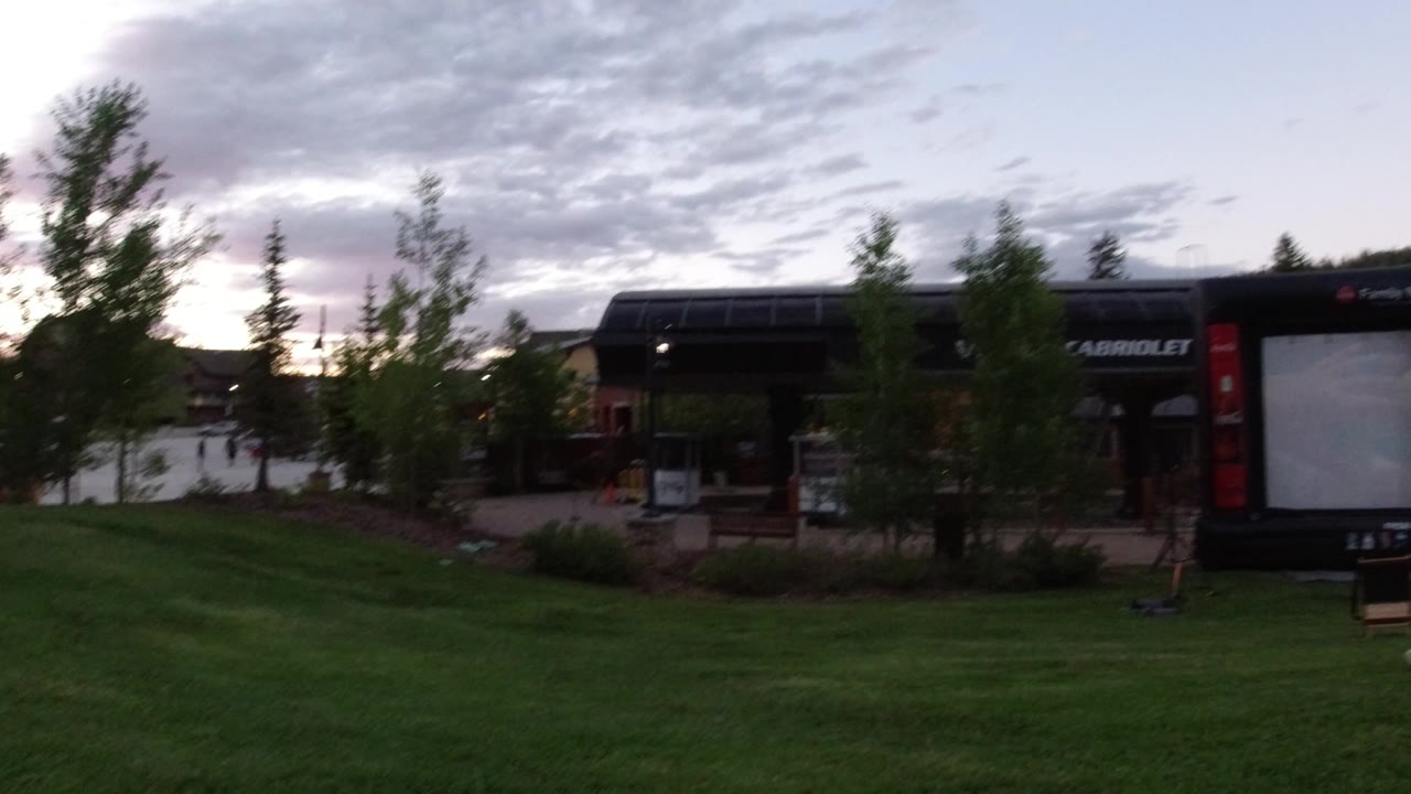 Grassy lawn facing an outdoor screen beside a dark roofed building.