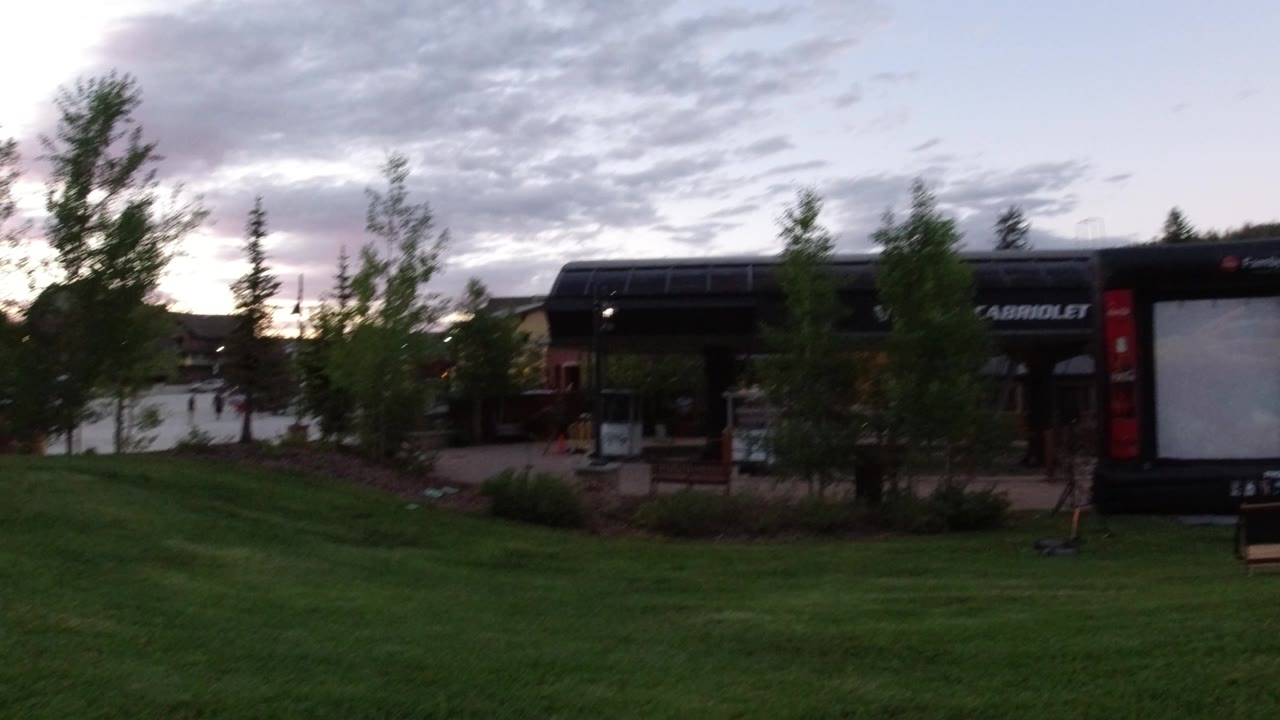 The Winter Park, Colorado scene holds on the grassy foreground, young trees, and a large screen beside the building, with no visible people in this moment.