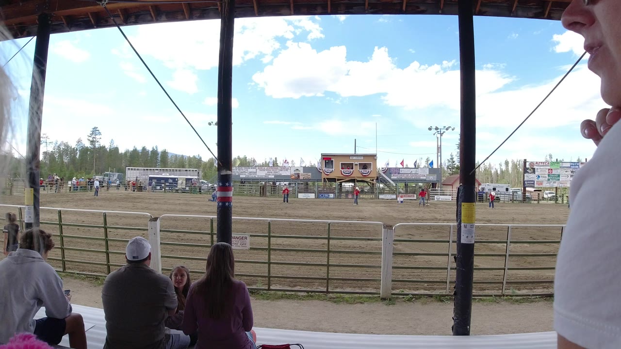 Covered bleachers looking toward a fenced dirt arena with spectators and event signs.