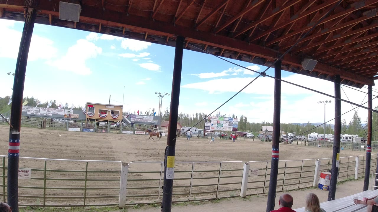 Wide dirt arena seen from covered bleachers with a horse and spectators.