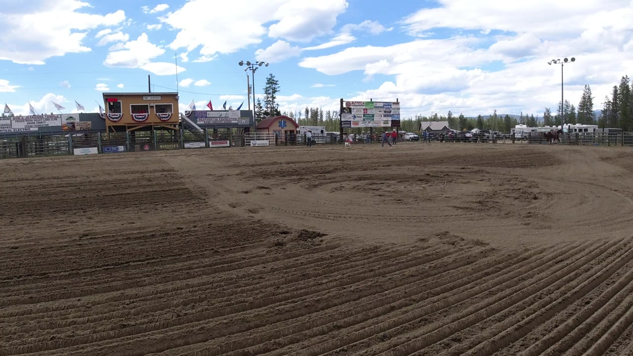 Wide dirt arena field with buildings and sky beyond.