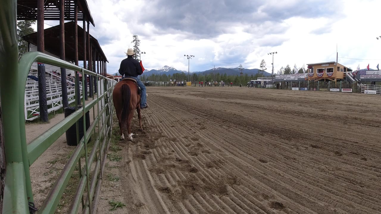 Cowboy on a brown horse beside a rodeo arena rail.
