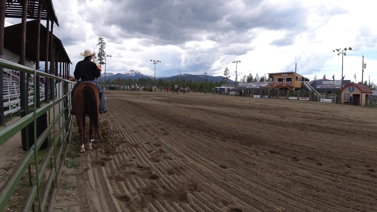 Cowboy on horseback beside a rodeo arena rail under cloudy sky.