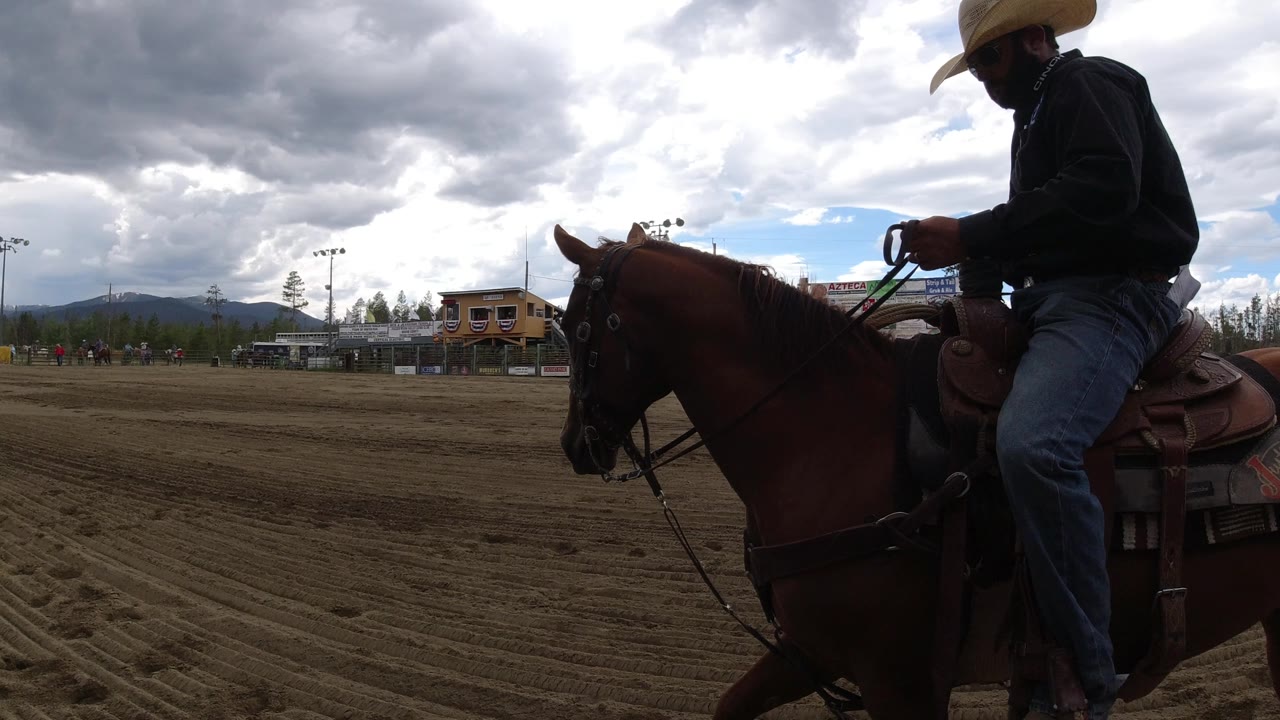 The rider remains close in profile on the horse beside the dirt track, with a green rail cutting across the top of the Winter Park, Colorado arena view.