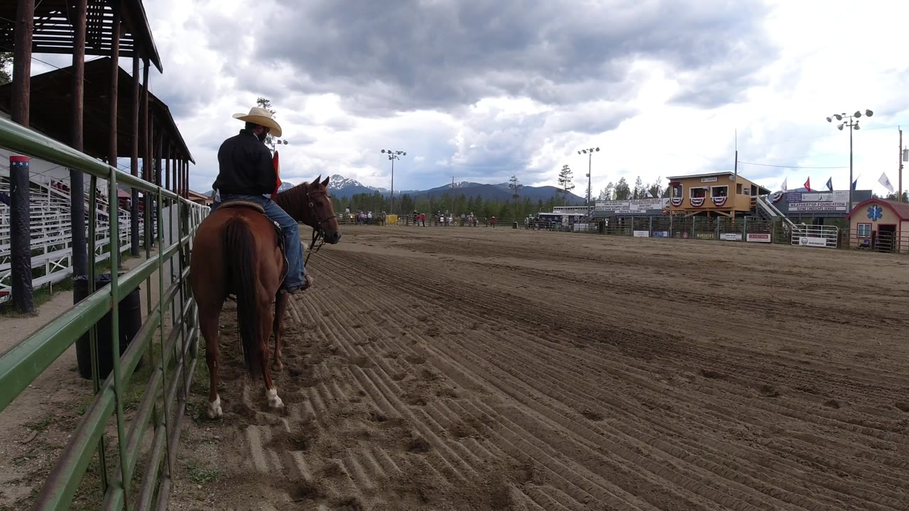 Cowboy-hatted rider on a brown horse beside an outdoor dirt arena.