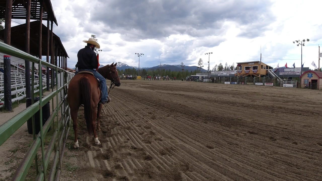 The horse and rider remain near the left rail of the Winter Park arena, with raked dirt tracks filling the foreground and a small building across the grounds.