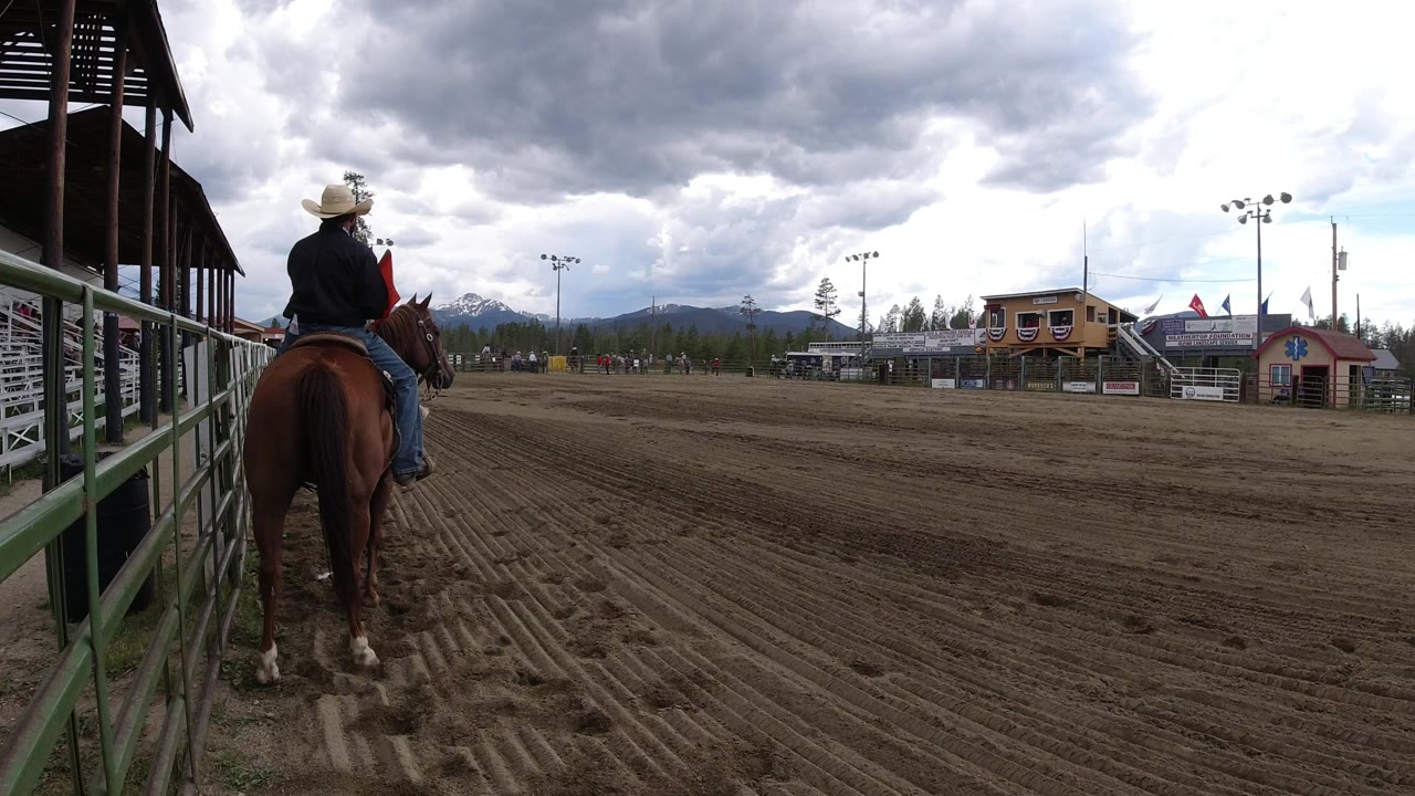 Rider on a brown horse beside railings at a dirt arena.