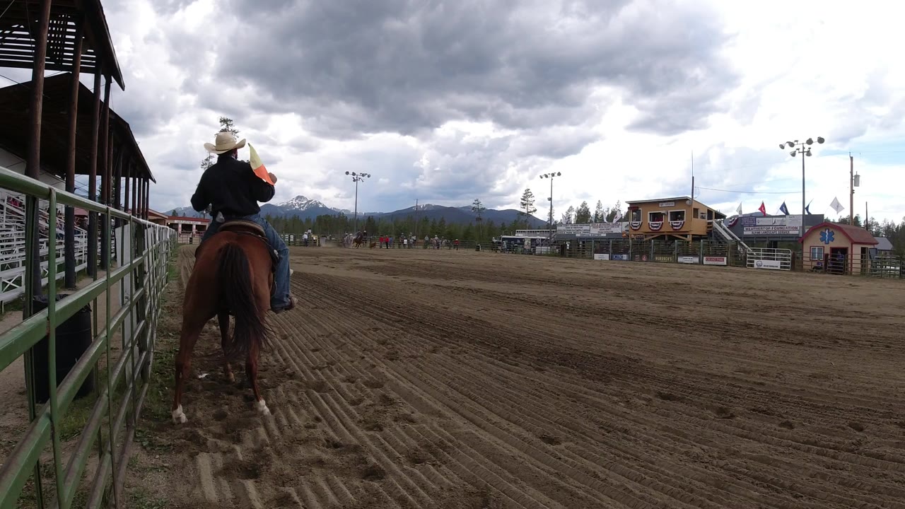 Rider on a horse beside arena railings under dark clouds.