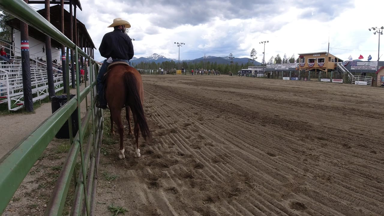 Cowboy-hatted rider on a brown horse beside a dirt arena rail.