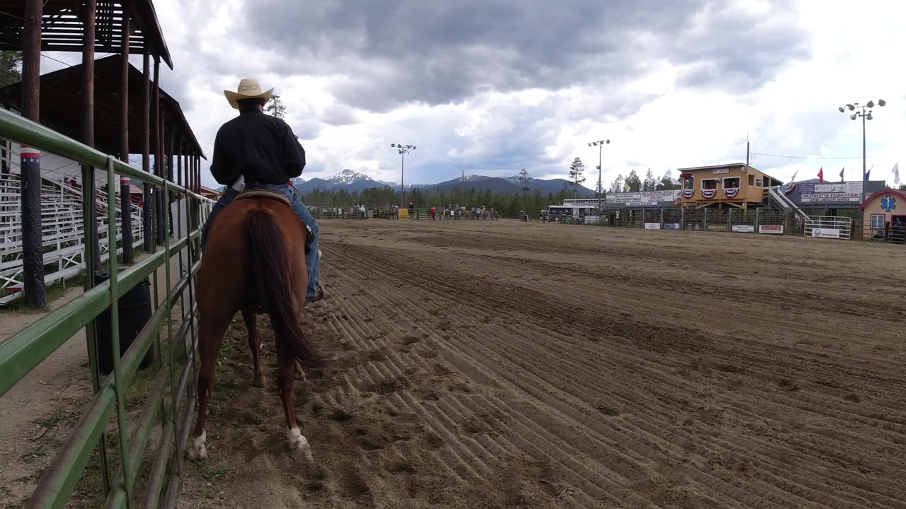 Back view of a cowboy on horseback in a rodeo arena.
