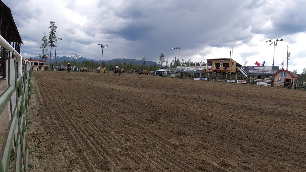 Wide dirt equestrian arena with distant riders and mountain backdrop.