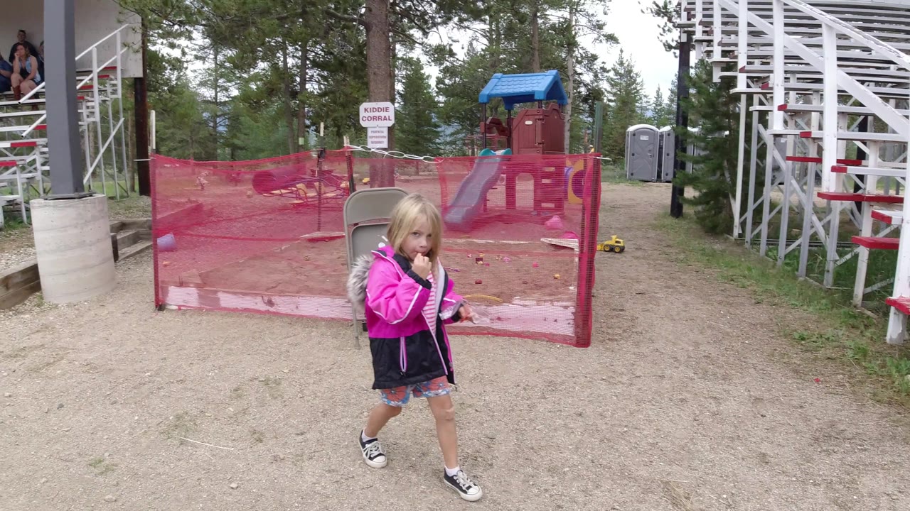 Girl walking beside red fencing and white bleachers.