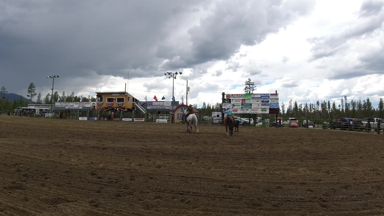 Rodeo arena with two horses farther apart under a bright break in clouds.