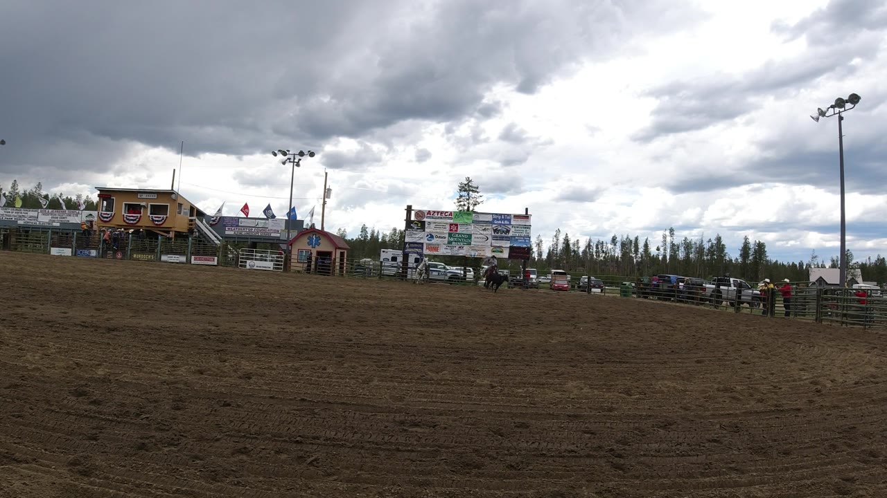 Horseback riders and dog near arena fence with cloudy sky.
