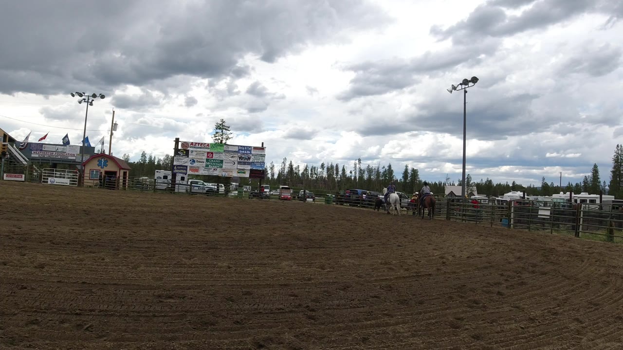 Wide dirt arena with horses near a fenced paddock under heavy clouds.