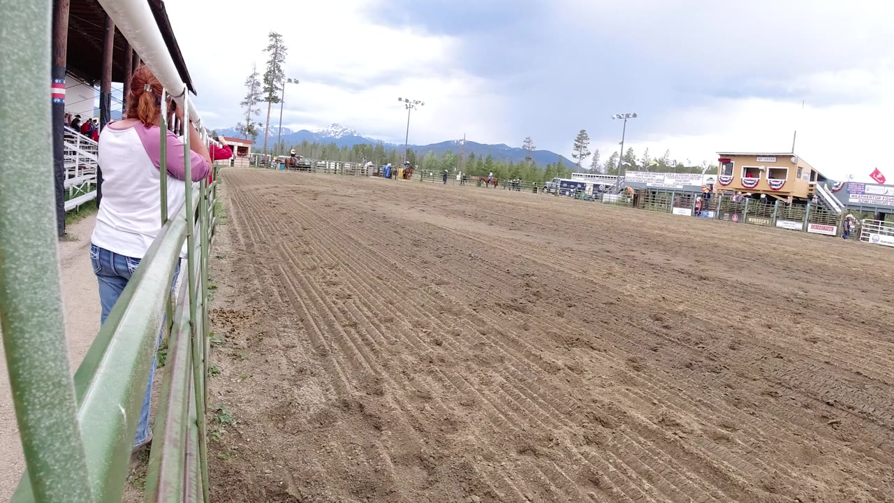 Dirt arena beside green railings under heavy clouds.