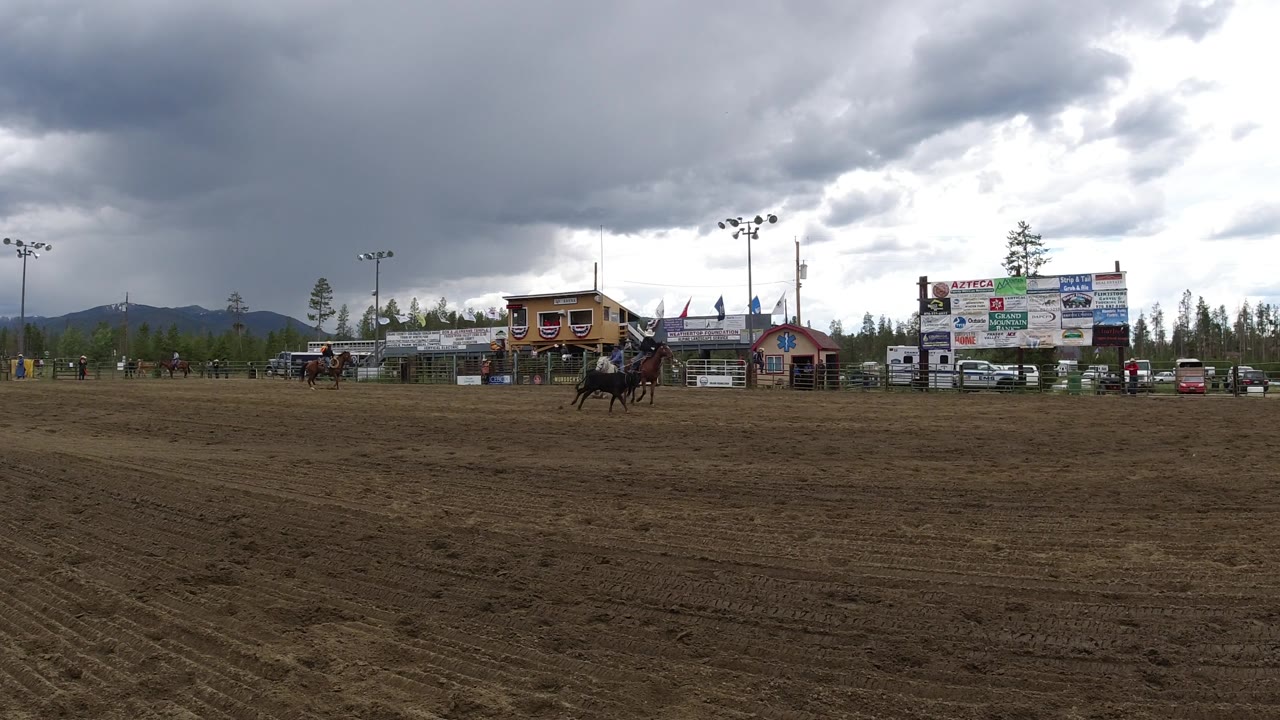Horseback rider crossing the right side of a rodeo arena near sponsor signs.