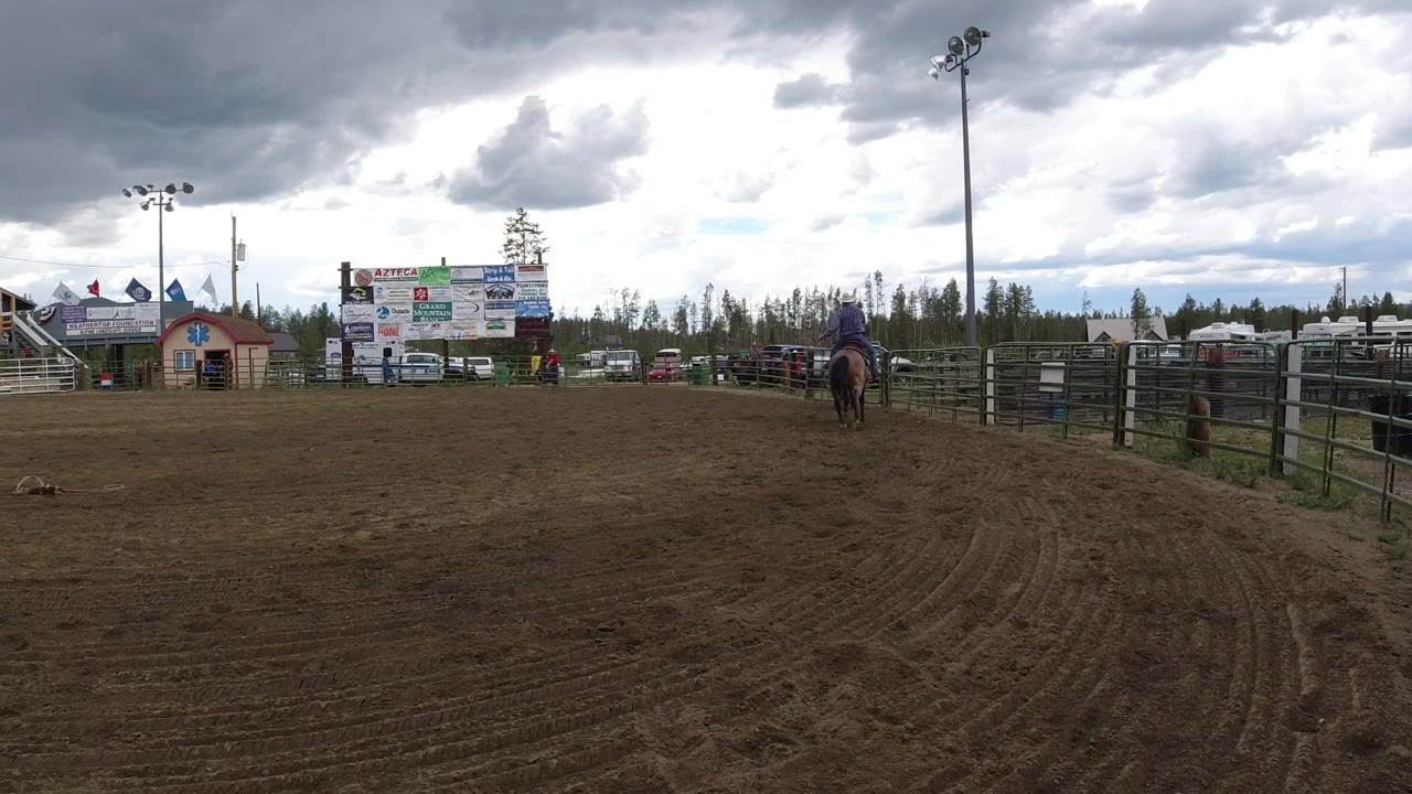 Wide dirt arena with a horse and rider near fencing under cloudy sky.