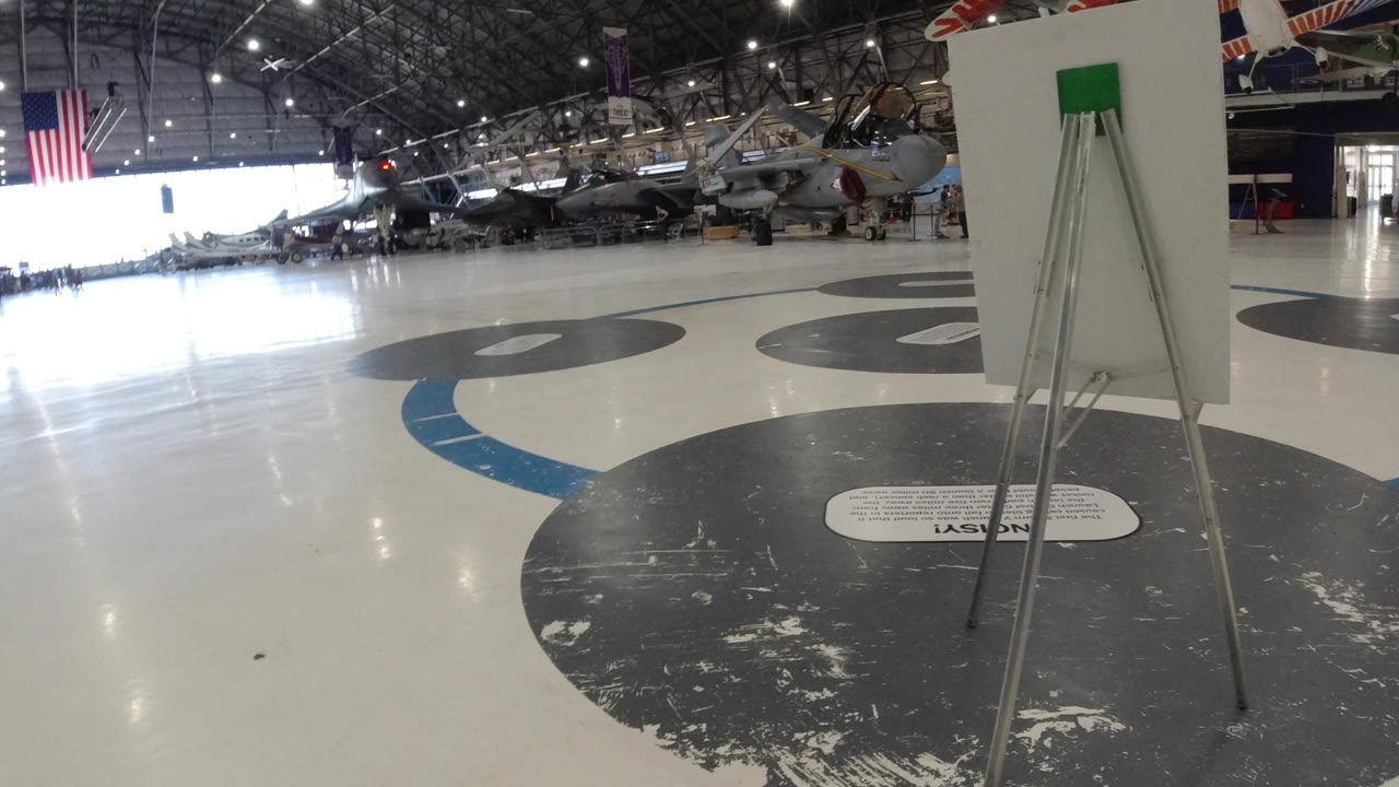 Wide hangar interior with aircraft displays and a signboard in the foreground.