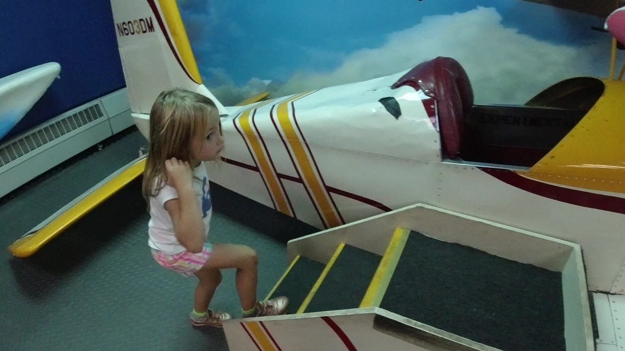 Young girl standing beside steps to an airplane-shaped play structure.