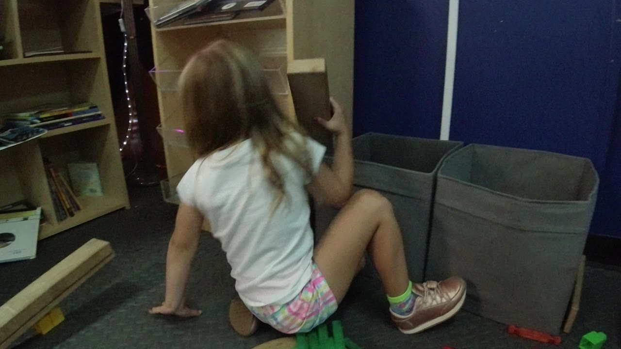 Blond child sitting on carpet beside wood pieces and storage bins.