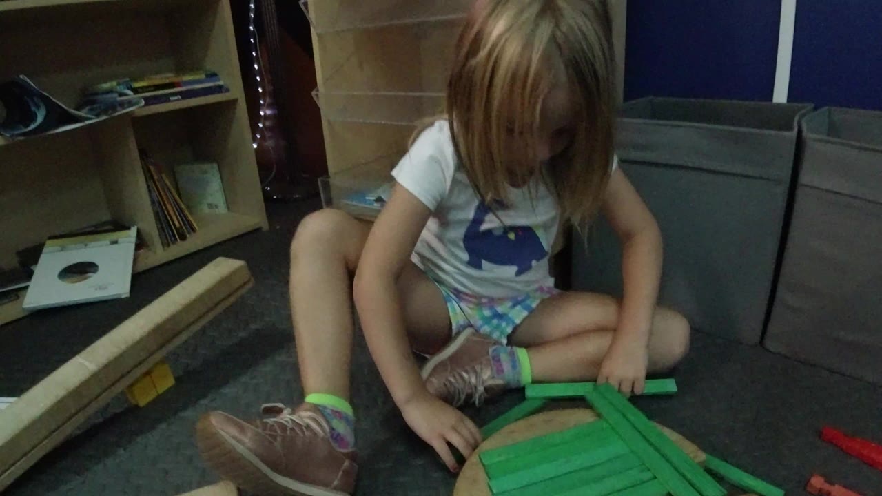 Young girl sits on the carpet and reaches toward green wooden blocks.