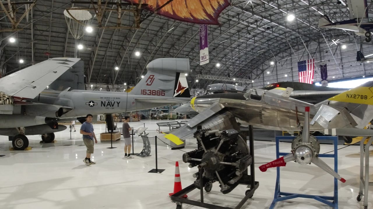 Grey aircraft tail, polished plane, and engine display in an aviation hangar.