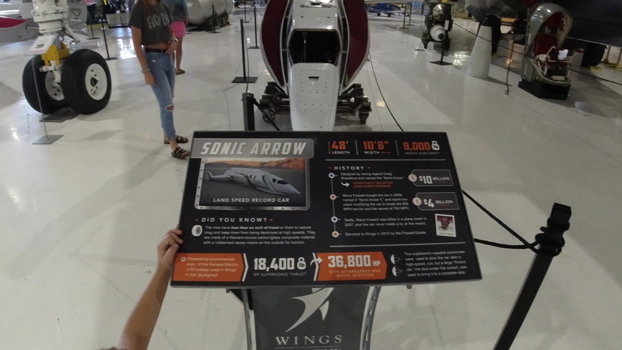 Sonic Arrow exhibit sign in front of a white aircraft nose and landing gear.