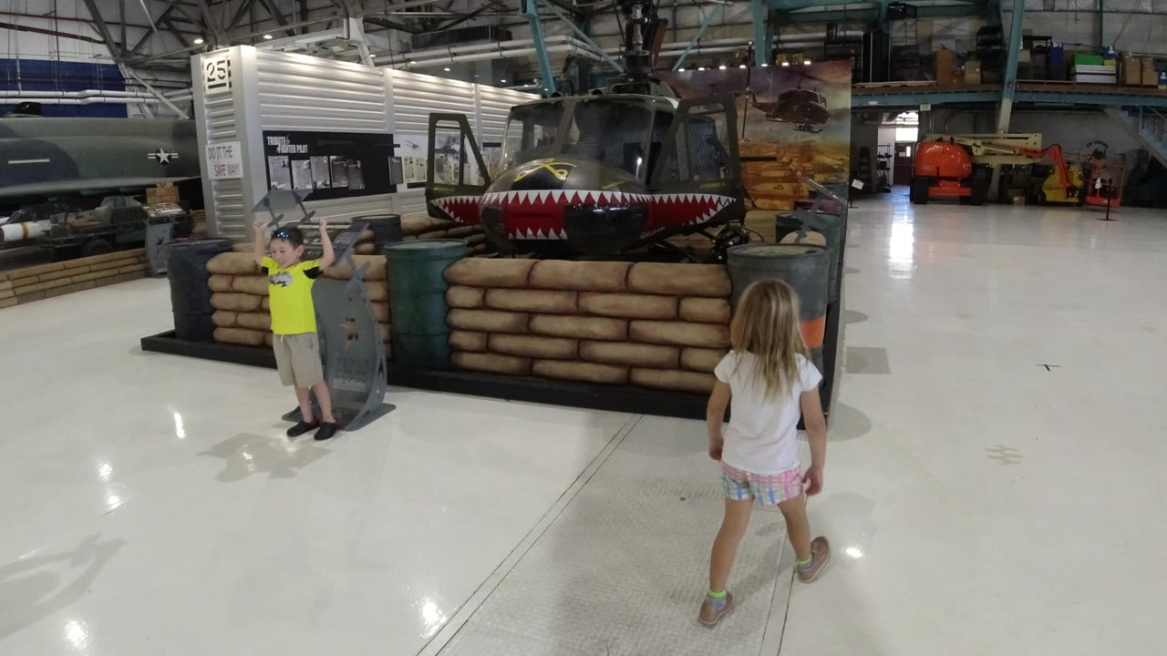 Girl walking toward a helicopter display inside a large hangar.